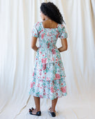 Woman wearing a floral dress against a white curtain background