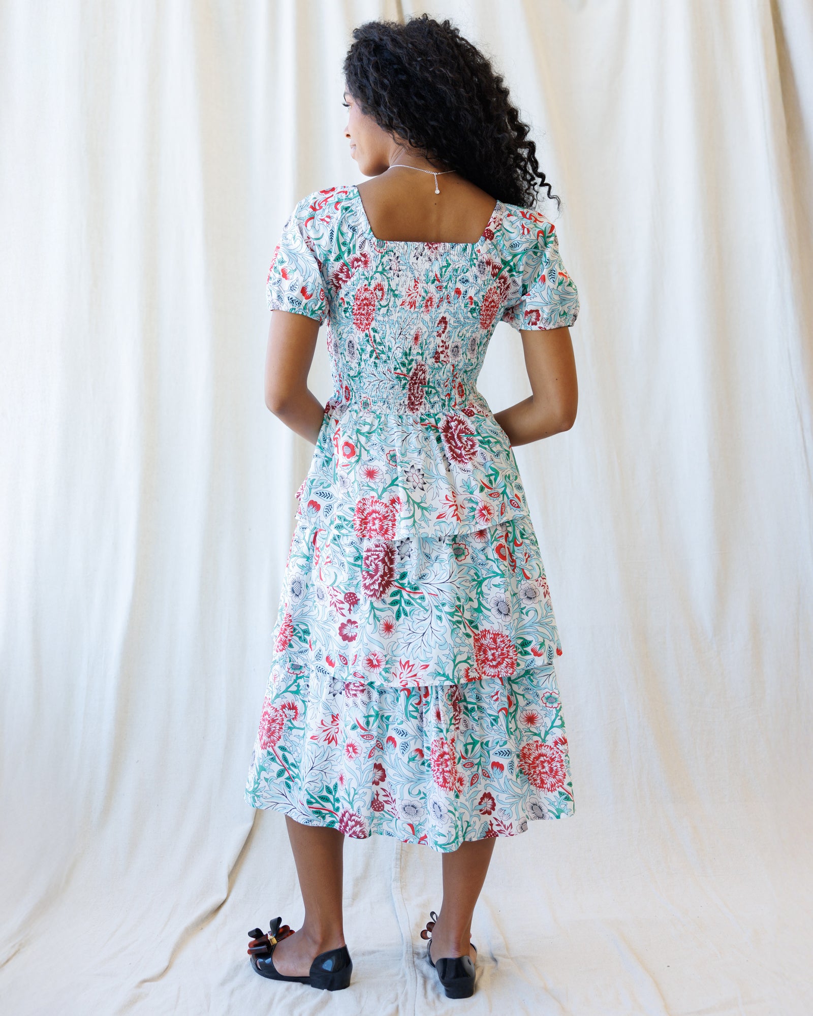 Woman wearing a floral dress against a white curtain background