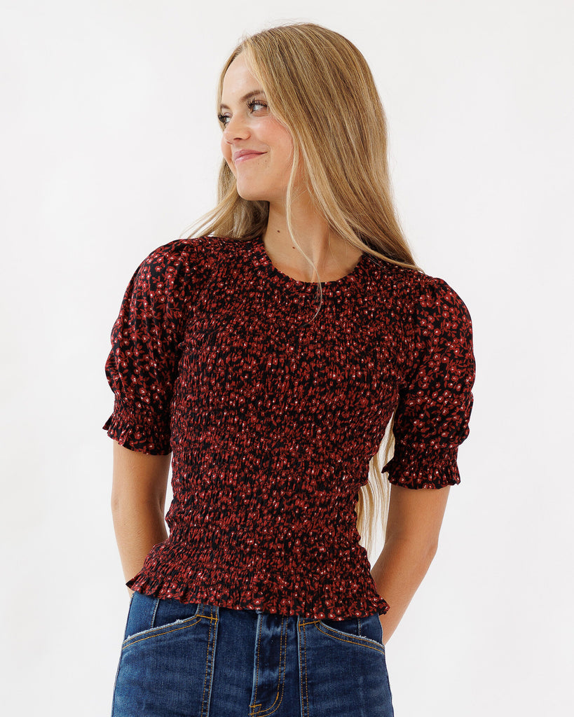 Woman wearing a red floral blouse with puffed sleeves on a white background