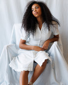 Woman in a light blue dress sitting on a white chair against a white background