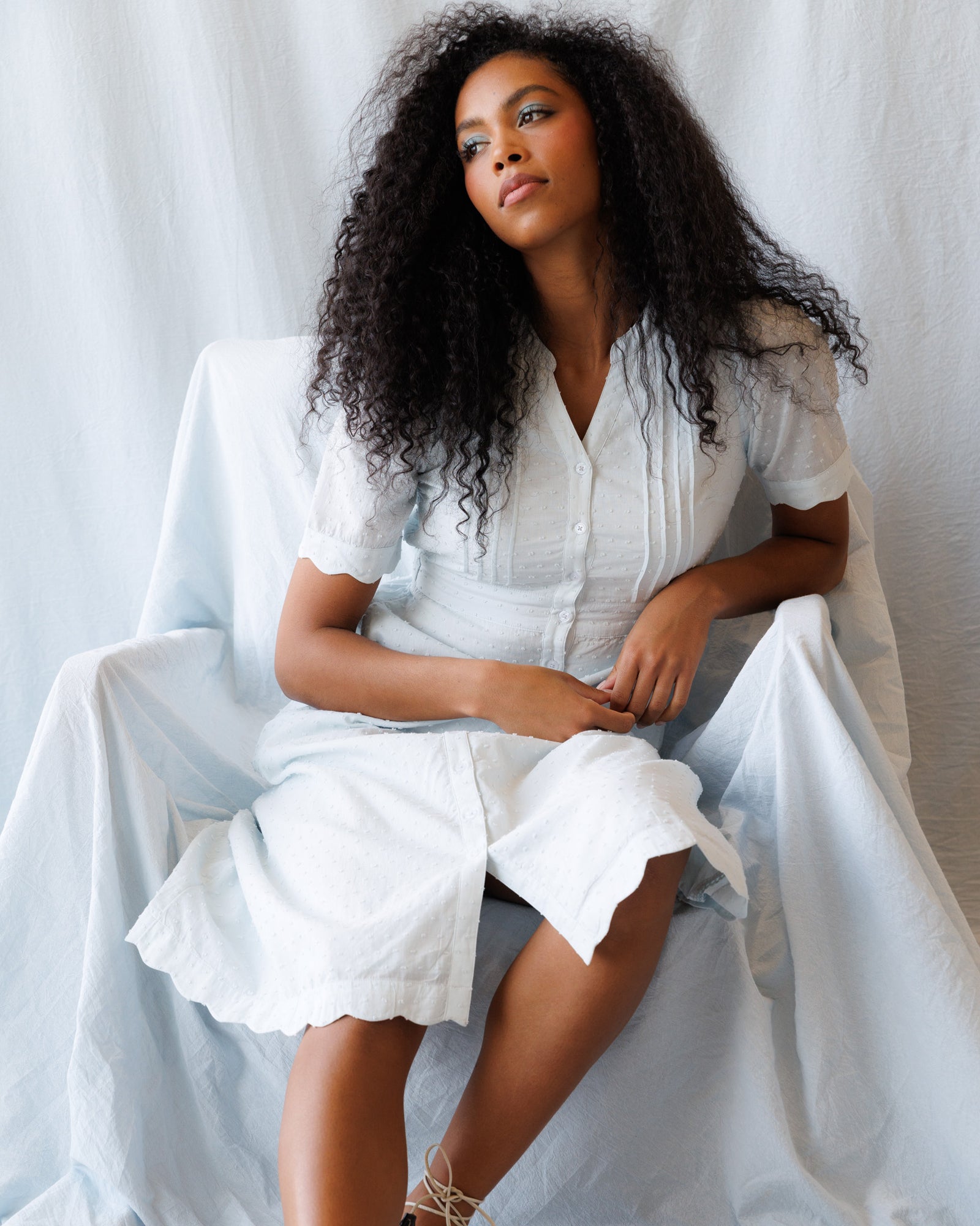 Woman in a light blue dress sitting on a white chair against a white background
