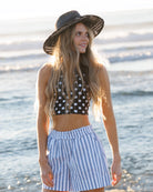 Woman wearing a polka dot top and striped shorts on a beach.