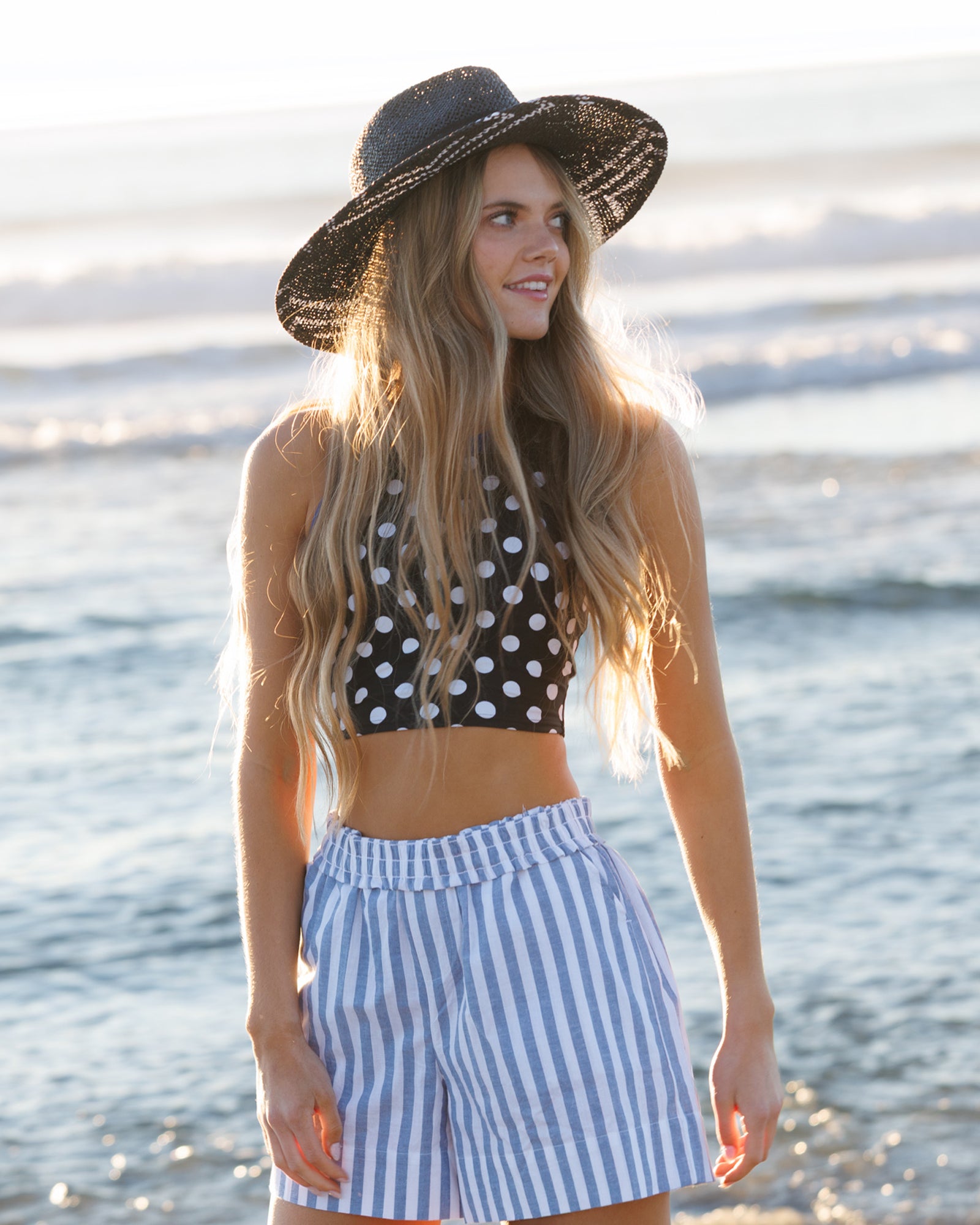 Woman wearing a polka dot top and striped shorts on a beach.