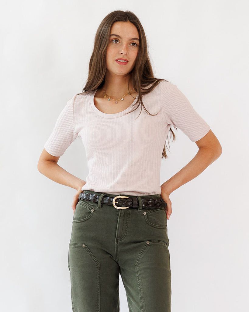 Woman wearing a light pink top and green pants against a white background