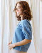 Woman wearing a blue denim shirt against a white curtain background