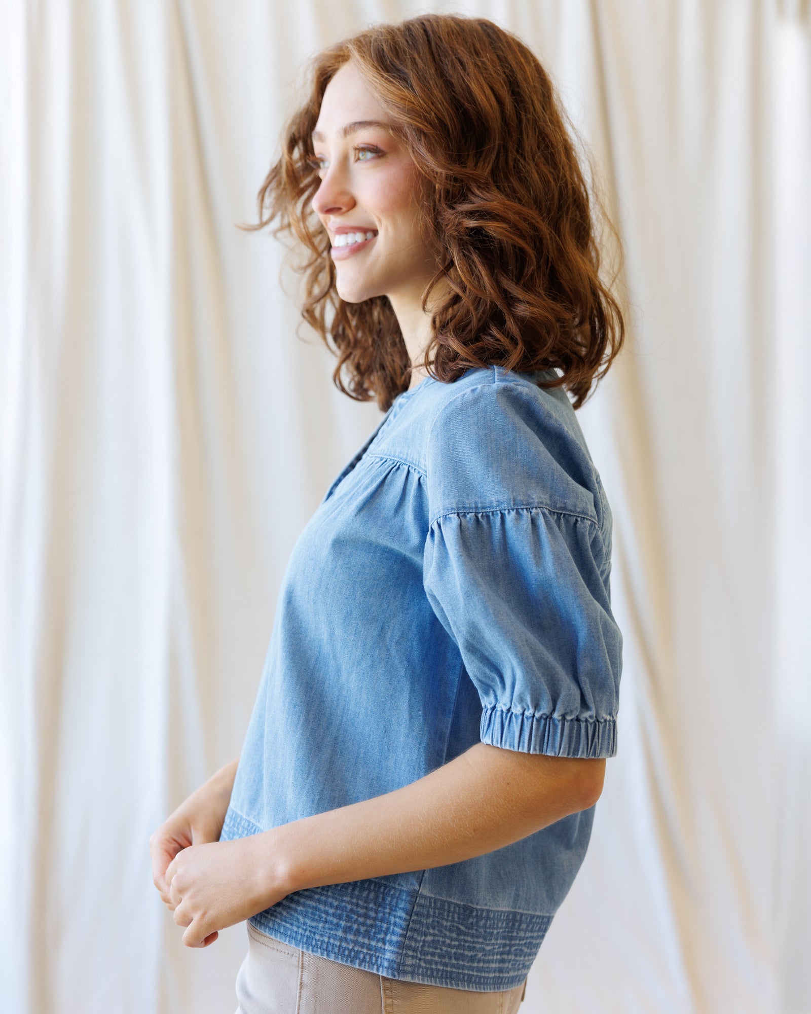 Woman wearing a blue denim shirt against a white curtain background