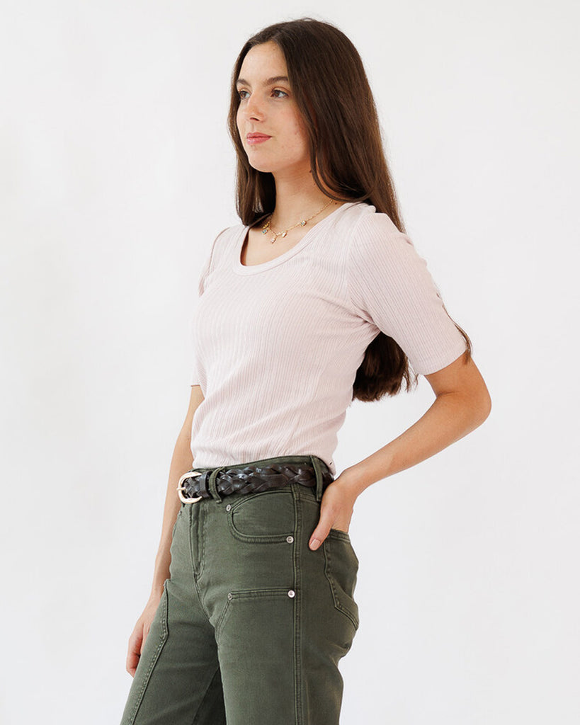 Woman wearing a light pink t-shirt and green pants against a white background