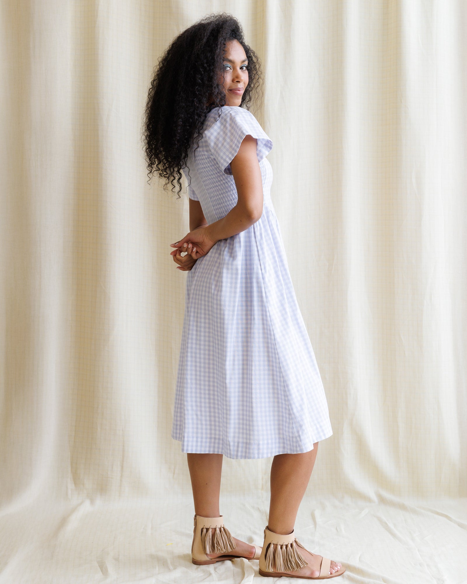Woman wearing a purple checkered dress standing against a plain background