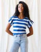 Woman wearing a blue and white striped shirt with ruffled sleeves against a plain background