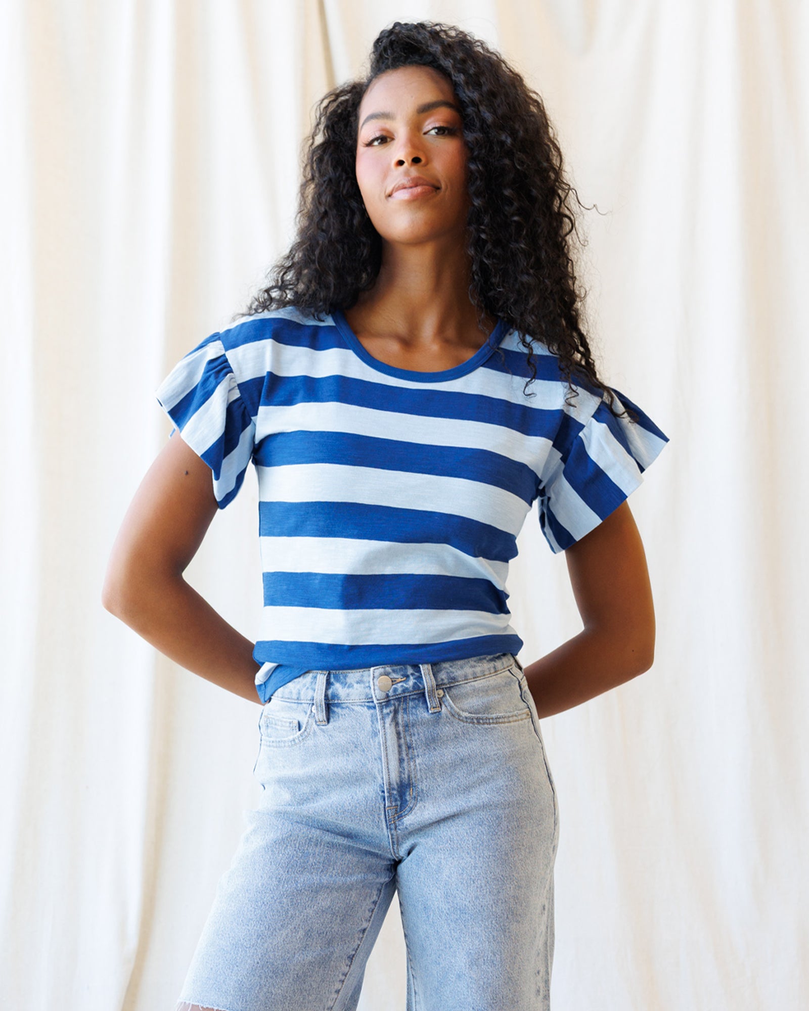Woman wearing a blue and white striped shirt with ruffled sleeves against a plain background