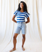 Woman wearing a blue and white striped shirt and denim shorts against a white curtain background