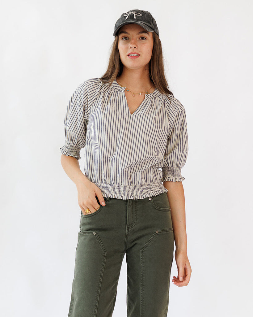 Woman wearing a striped blouse and green pants with a cap on a white background