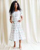 Woman wearing a white dress with green floral pattern against a plain background