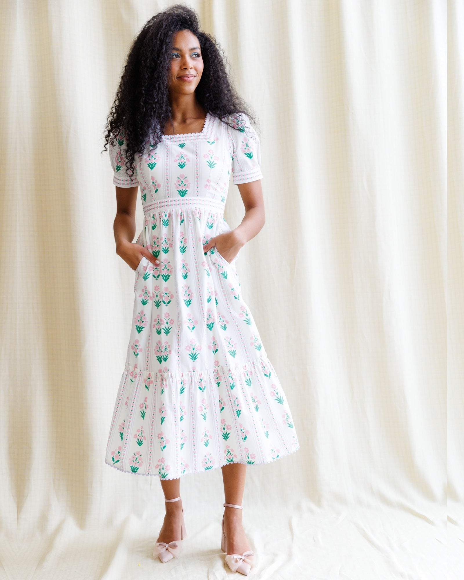 Woman wearing a white dress with green floral pattern against a plain background