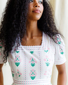 Woman wearing a white blouse with floral embroidery in a softly lit indoor setting