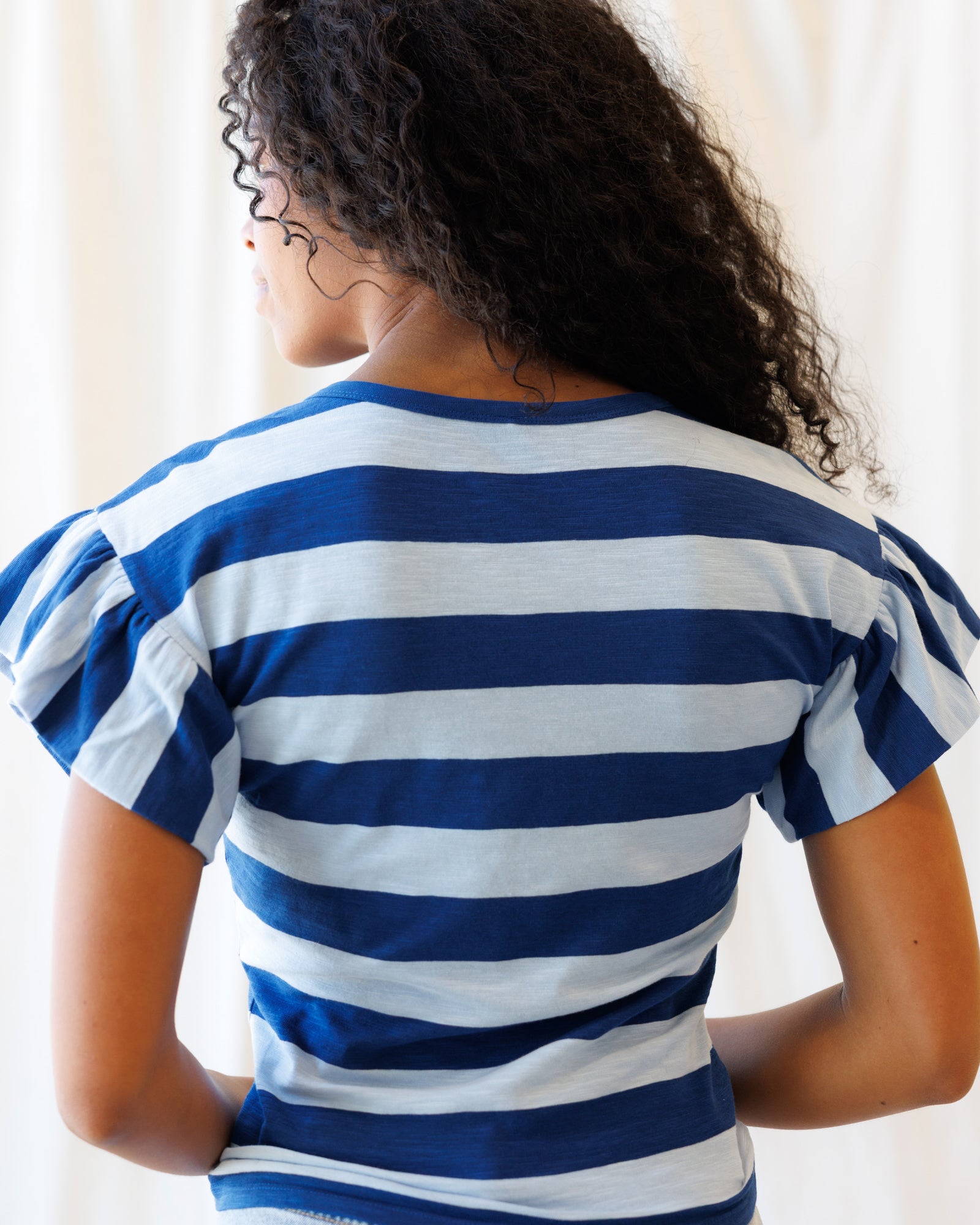Person wearing a blue and white striped shirt with ruffled sleeves.