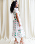 Woman wearing a white dress with floral pattern against a plain background