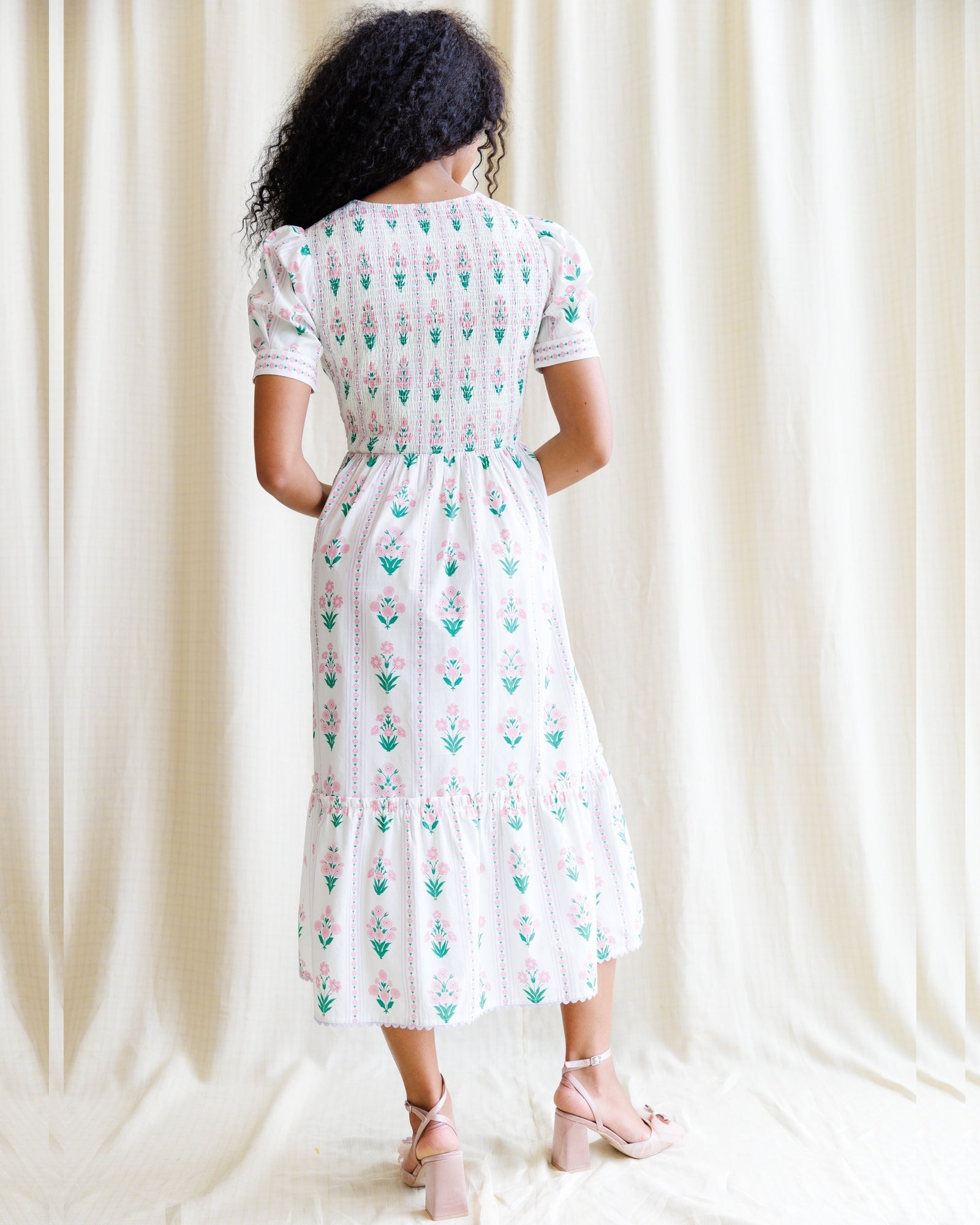 Woman wearing a white dress with green floral pattern against a white curtain background