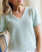 Woman wearing a light green crochet top with a blurred background