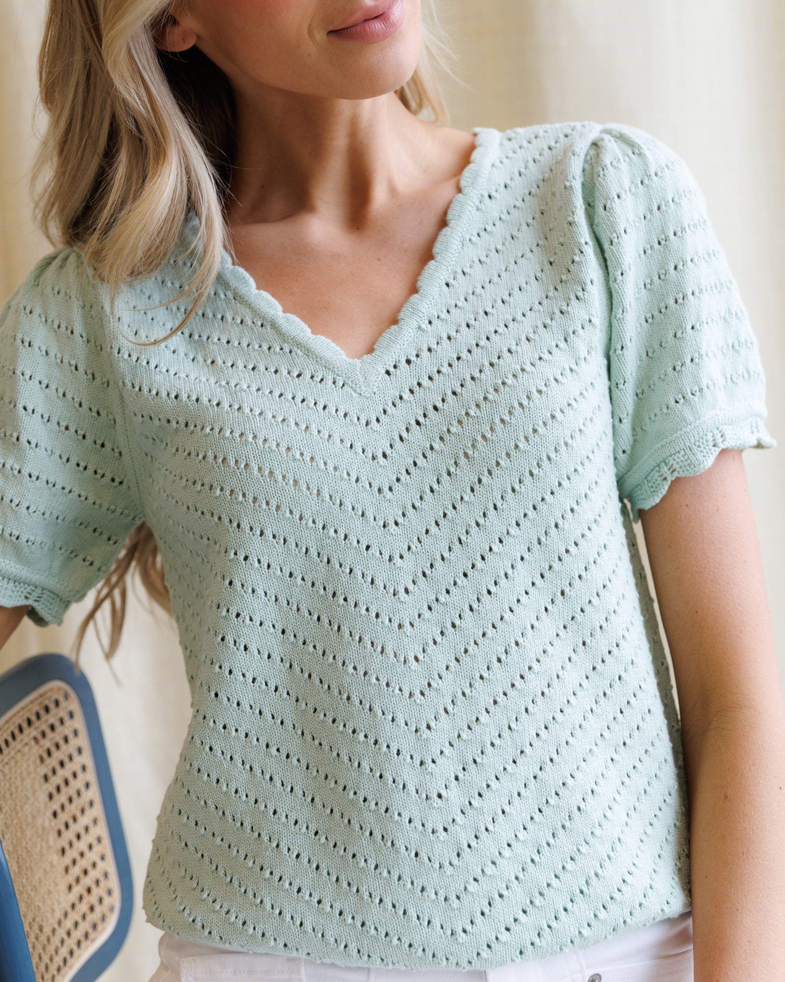 Woman wearing a light green crochet top with a blurred background
