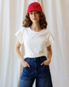 Woman wearing a white t-shirt, blue jeans, and a red cap against a plain background