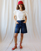 Person wearing a white t-shirt, blue denim shorts, and red cap against a plain background