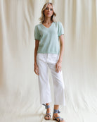 Woman wearing a light green knitted top and white pants against a plain background