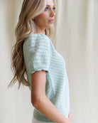 Woman wearing a light green knitted top against a neutral background