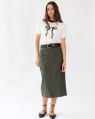 Woman wearing a white top with black bow and green skirt on a white background