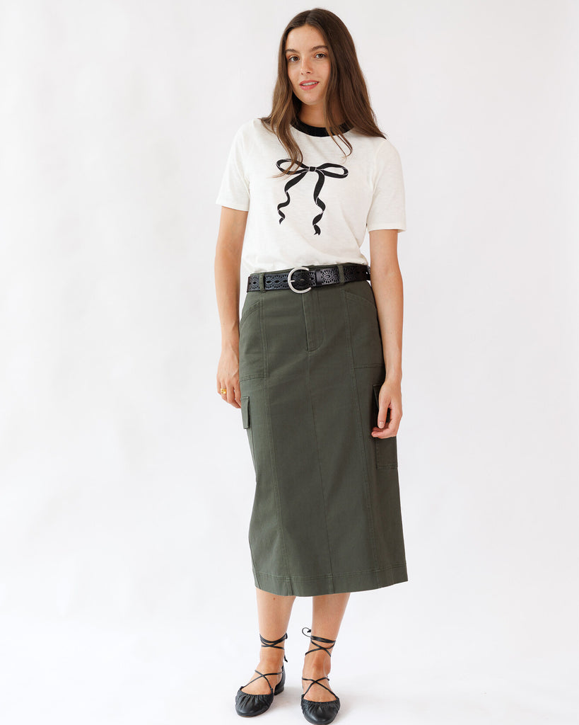 Woman wearing a white top with black bow and green skirt on a white background