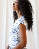 Woman wearing a white top with blue floral patterns against a neutral background