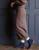 A person wearing a ribbed brown midi skirt, matching sweater, cream socks, and navy ankle boots with brown heels, standing against a dark blue paneled wall.
