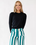 Woman wearing a black top and green and white striped pants on a white background