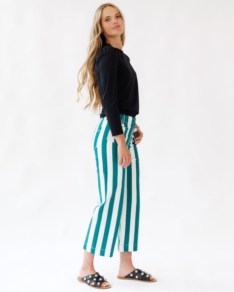 Woman wearing black top and green and white striped pants on a white background