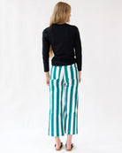 Woman wearing black long-sleeve top and green and white striped pants on a white background
