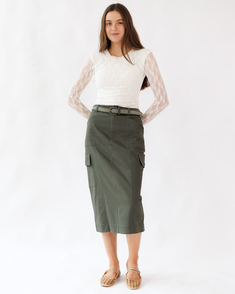 Woman wearing a white lace top and green cargo skirt on a white background