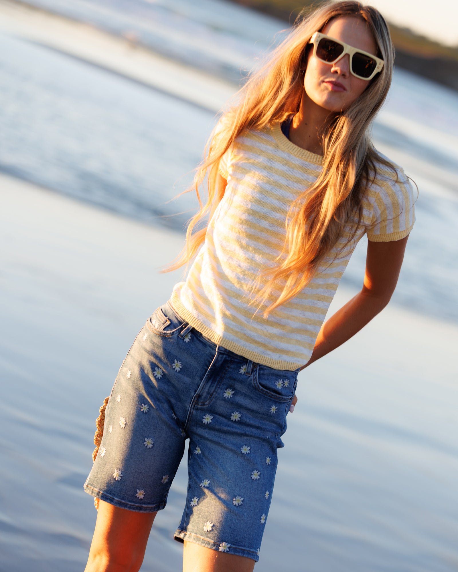 Woman wearing a striped shirt and denim shorts by a body of water.