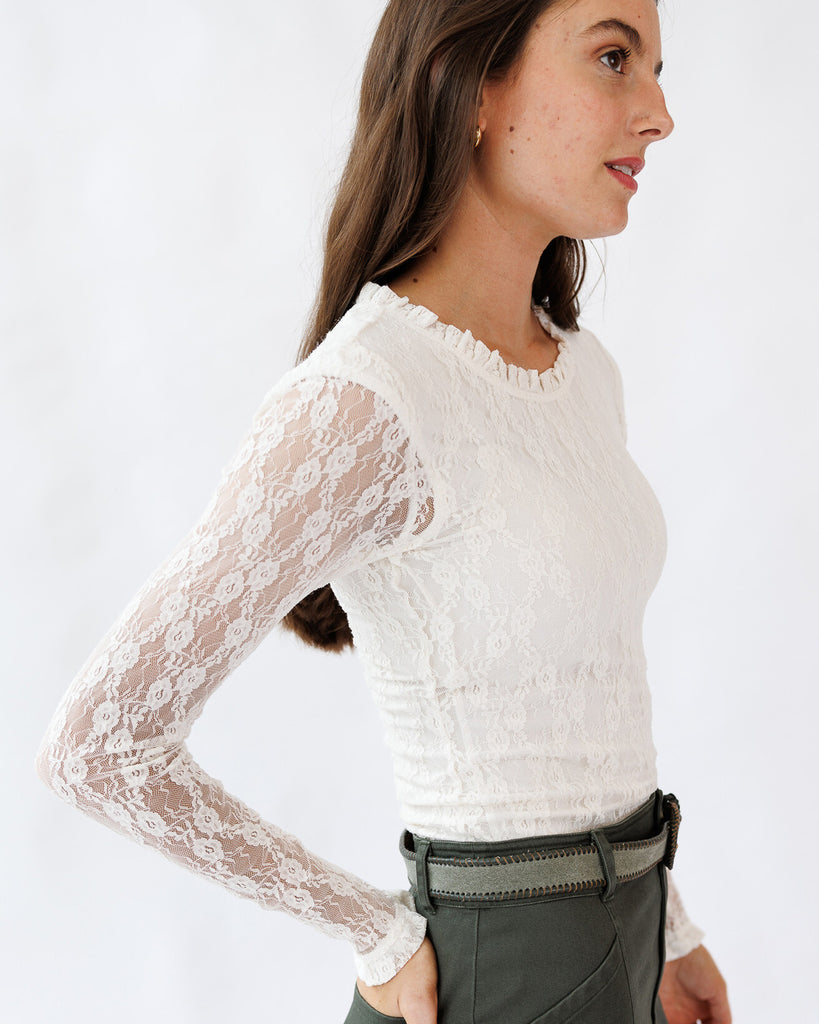Woman wearing a white lace long-sleeve top against a plain background