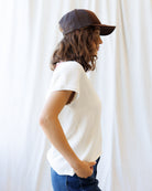 Person wearing a white t-shirt and dark cap against a white curtain background