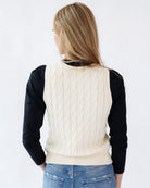 Person wearing a cream cable knit vest over a black long-sleeve shirt on a white background