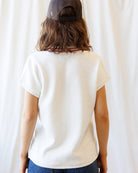 Person wearing a white t-shirt and dark cap from behind against a plain background