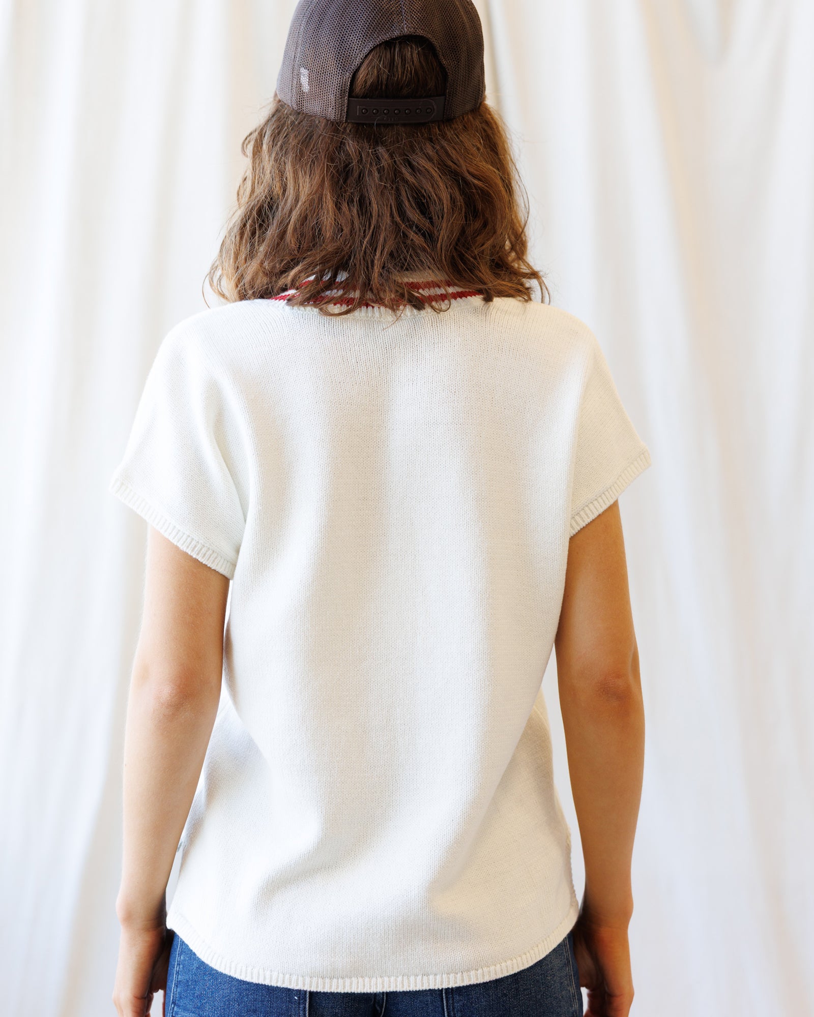 Person wearing a white t-shirt and dark cap from behind against a plain background