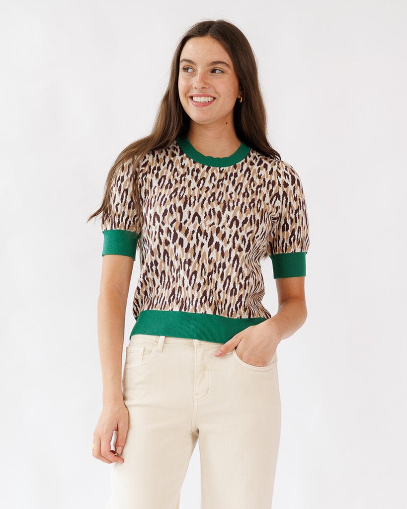 Woman wearing a leopard print top with green trim on a white background