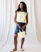 Woman holding a yellow and white striped bag against a plain background