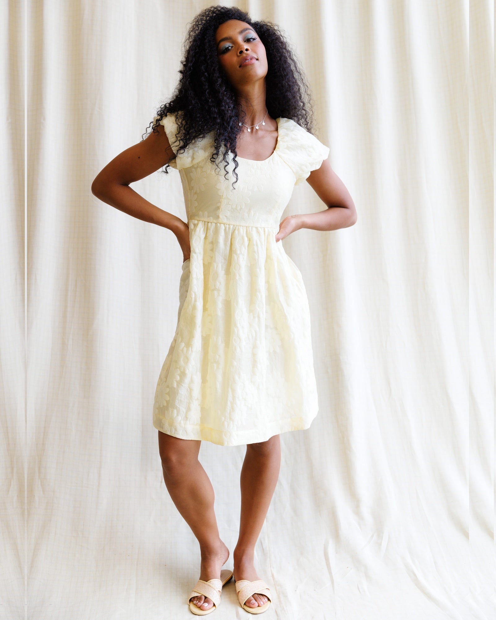 Woman wearing a white dress with ruffled sleeves against a white curtain background