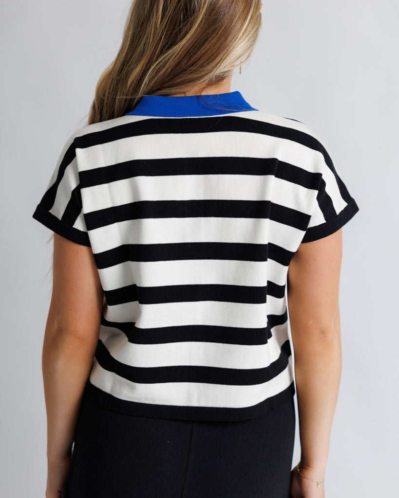 Model wearing a black and white striped short sleeve polo with a blue collar