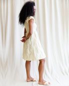 Woman wearing a light-colored dress standing against a white curtain