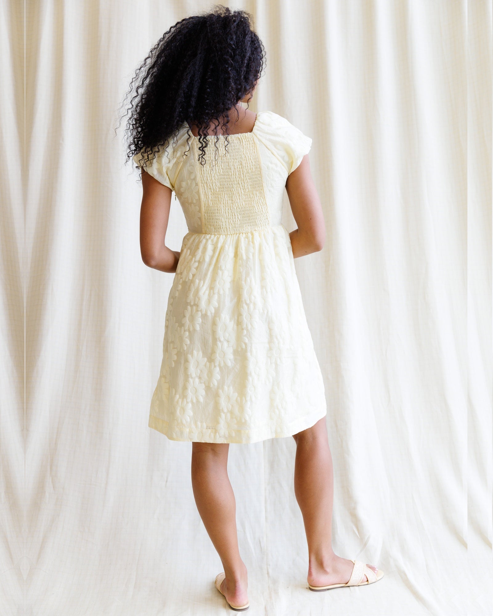 Person wearing a yellow dress standing in front of white curtains