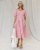 Image of a woman wearing a white and red striped midi dress with hands in front pockets
