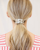 Person with blonde hair tied into a ponytail with a silver hair tie against a light background